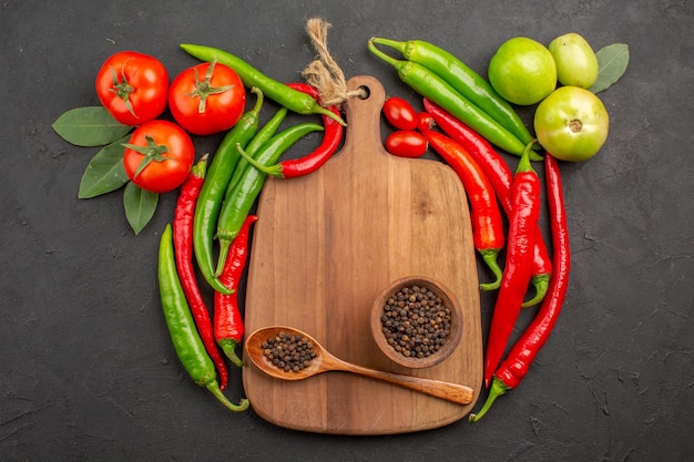 Vue de dessus tomates poivrons rouges et verts chauds bol de poivre noir et cuillère sur une planche à découper sur fond noir avec espace libre