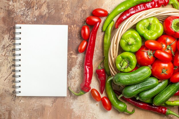 Vue de dessus tomates poivrons verts et rouges dans un panier en osier légumes un cahier sur fond ambre