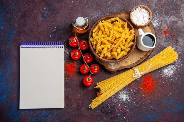 Vue de dessus des tomates rouges fraîches avec des pâtes italiennes crues sur le sombre bureau alimentaire repas de pâtes salade crue