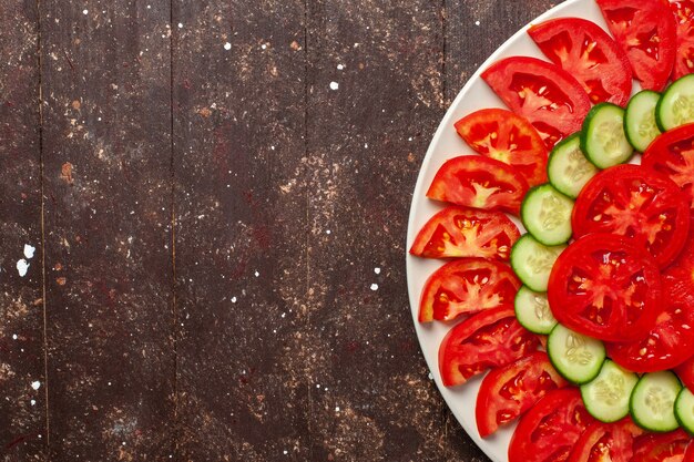 Vue de dessus tomates rouges fraîches tranchées avec des concombres salade fraîche sur un bureau brun