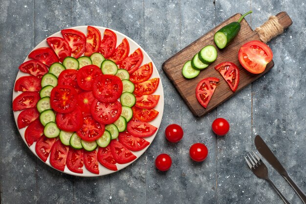 Vue de dessus tomates rouges fraîches en tranches de salade fraîche sur un bureau gris rustique