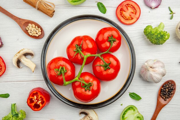 Vue de dessus tomates rouges sur plaque blanche champignons à l'ail anis poivrons noirs dans une cuillère en bois sur fond gris