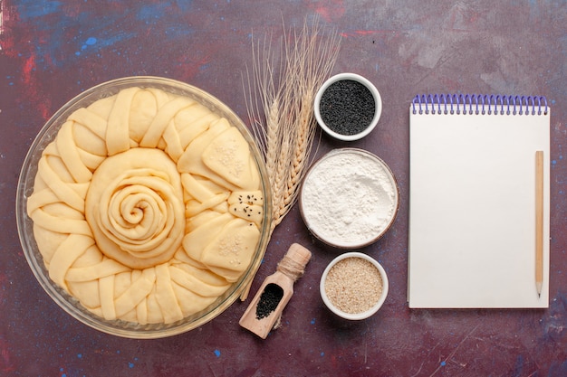 Vue de dessus tour de tarte cru formé avec des assaisonnements et bloc-notes sur un bureau violet foncé