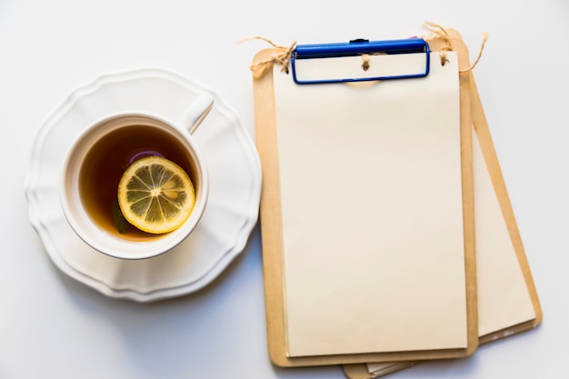 Une vue de dessus d&#39;une tranche de citron dans une tasse de thé près du presse-papiers en bois sur fond blanc