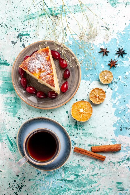 Vue de dessus tranche de gâteau avec cornouiller rouge frais et tasse de thé sur une surface bleue gâteau aux fruits cuire tarte au sucre biscuit sucré