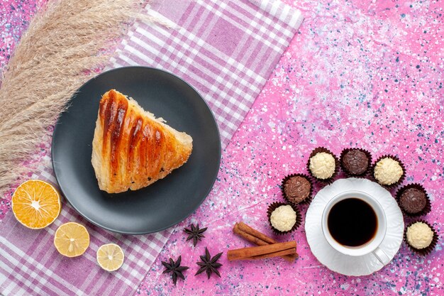 Vue de dessus de la tranche de pâtisserie avec tasse de thé à la cannelle et bonbons au chocolat sur la surface rose