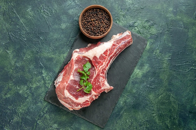 Vue de dessus tranche de viande fraîche avec du poivre sur fond bleu foncé cuisine animal vache poulet nourriture couleur viande de boucher