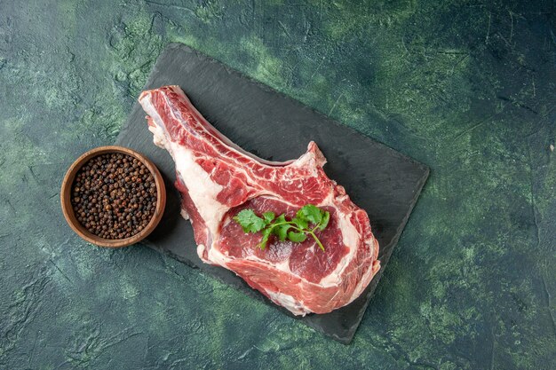 Vue de dessus tranche de viande fraîche avec du poivre sur fond bleu foncé cuisine animal vache poulet nourriture couleur viande de boucher