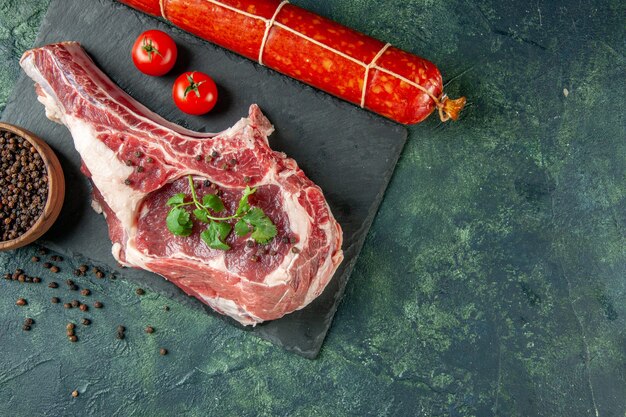 Vue de dessus tranche de viande fraîche avec du poivre et des saucisses sur fond bleu foncé cuisine animal vache poulet nourriture couleur viande de boucher