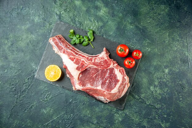 Vue de dessus tranche de viande fraîche avec des tomates rouges sur fond bleu foncé cuisine animal vache nourriture boucher couleur de la viande