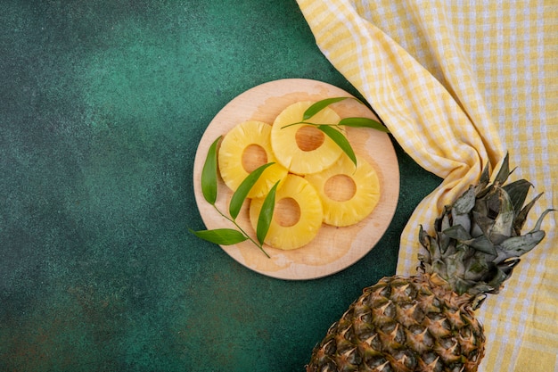 Photo gratuite vue de dessus des tranches d'ananas et d'ananas sur tissu à carreaux et surface verte