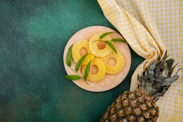 Vue de dessus des tranches d'ananas et d'ananas sur tissu à carreaux et surface verte