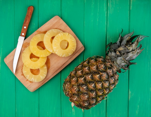 Photo gratuite vue de dessus des tranches d'ananas et couteau sur une planche à découper avec un tout sur une surface verte