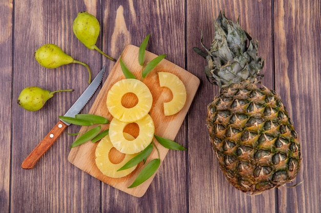 Vue De Dessus Des Tranches D'ananas Avec Des Feuilles Sur Une Planche à Découper Et Pêche Ananas Avec Un Couteau Sur Une Surface En Bois