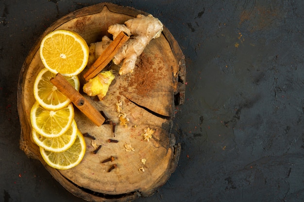 Vue de dessus de tranches de citron bâtons de cannelle et gingembre sur une planche de bois sur fond noir