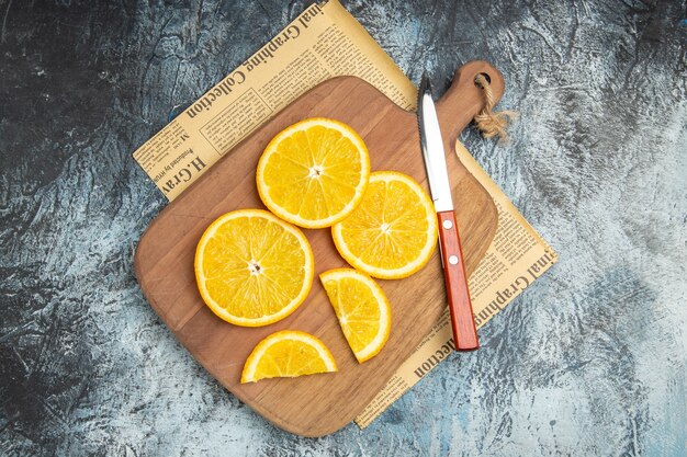 Vue de dessus des tranches de citron frais avec un couteau sur une planche à découper en bois sur du papier journal sur fond gris