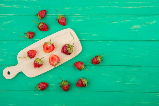 Vue de dessus des tranches et des fraises entières sur une planche de cuisine en bois sur un fond en bois vert avec espace copie