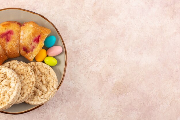 Une vue de dessus des tranches de gâteau aux cerises avec des bonbons et des biscuits sur le sucre biscuit gâteau de bureau rose