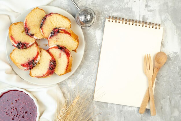 Vue de dessus des tranches de gâteau à la confiture sur une assiette de confiture dans un bol une cuillère en bois croisée et un cahier de fourchette sur la table