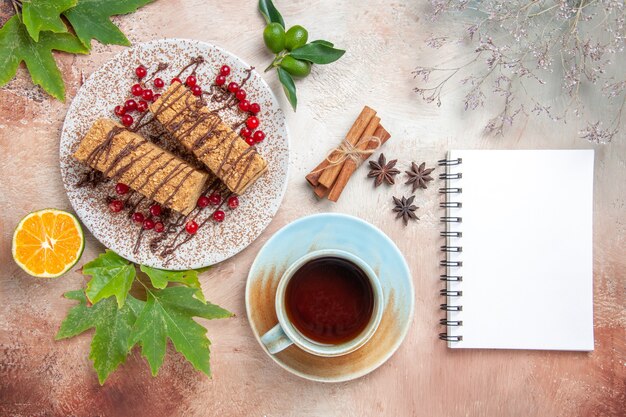 Vue de dessus des tranches de gâteau avec une tasse de thé et des baies rouges à la lumière