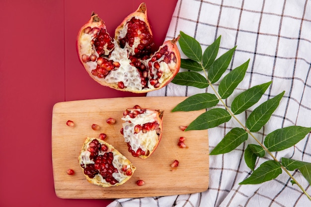 Vue de dessus des tranches de grenade exotiques avec des graines rouges sur planche de cuisine en bois avec feuille verte sur nappe à carreaux sur rouge