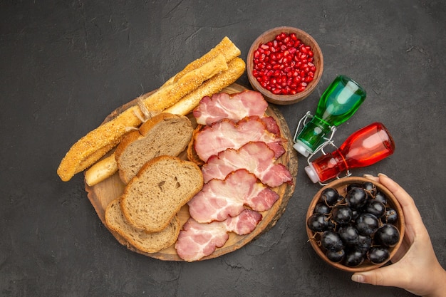 Photo gratuite vue de dessus des tranches de jambon frais avec du pain aux fruits et des petits pains sur fond sombre