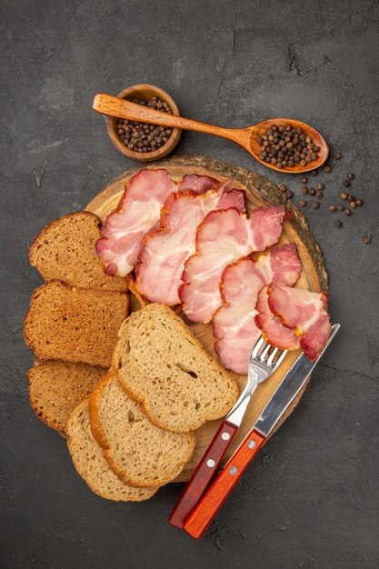 Vue de dessus des tranches de jambon frais avec des petits pains et des tranches de pain sur fond sombre