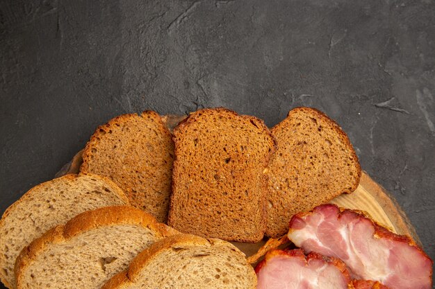 Vue de dessus des tranches de jambon frais avec des petits pains et des tranches de pain sur fond sombre