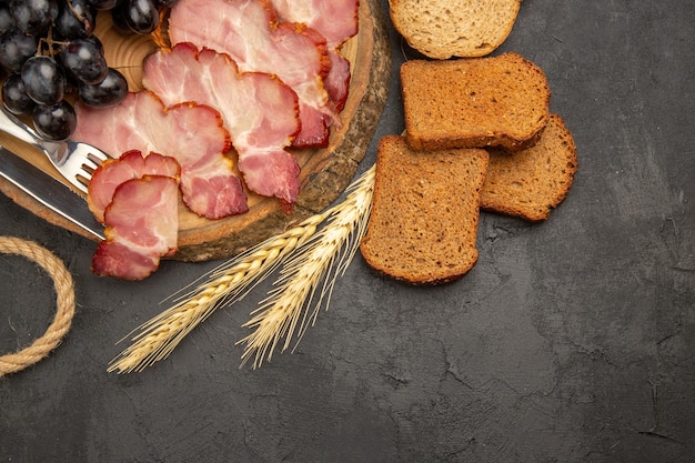 Vue de dessus des tranches de jambon avec des raisins et des tranches de pain sur fond sombre