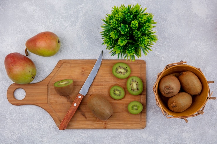 Photo gratuit vue de dessus des tranches de kiwi avec un couteau sur une planche à découper et dans un panier avec des poires sur fond blanc