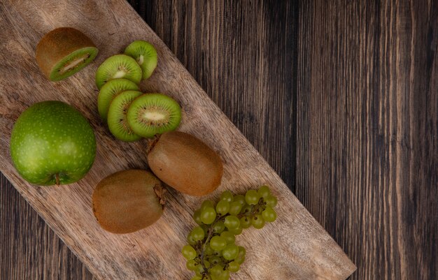 Vue de dessus des tranches de kiwi avec pomme verte et raisins sur un support sur un fond en bois