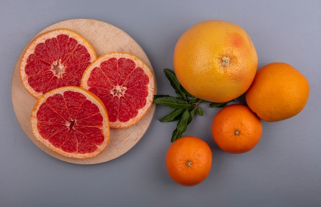 Photo gratuite vue de dessus des tranches de pamplemousse sur un support avec des oranges sur fond gris