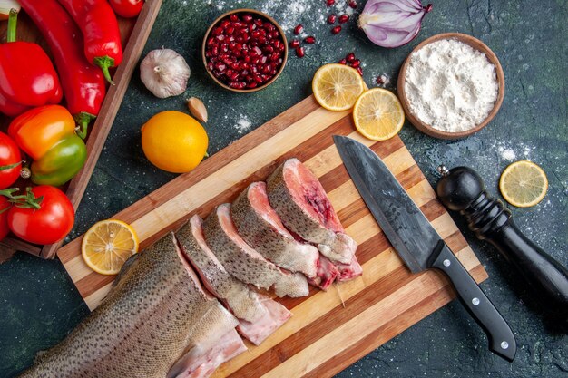 Vue de dessus tranches de poisson cru couteau sur planche à découper légumes sur planche de service en bois sur table de cuisine