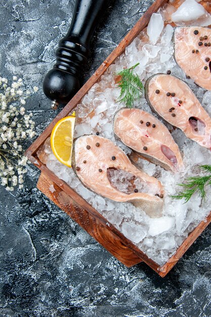 Vue de dessus des tranches de poisson cru avec de la glace sur un moulin à poivre en planche de bois sur une table