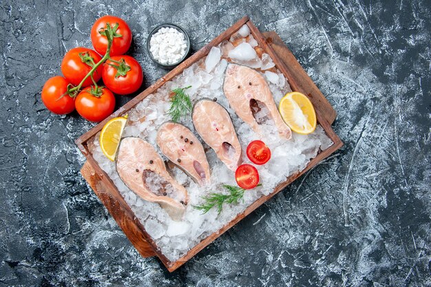 Vue de dessus des tranches de poisson cru avec de la glace sur planche de bois tomates sel de mer sur table avec espace libre