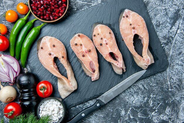 Vue de dessus des tranches de poisson cru sur des légumes de couteau de tableau noir sur fond gris