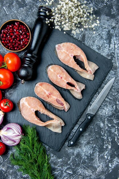 Vue de dessus des tranches de poisson cru sur tableau noir aneth graines de grenade tomates moulin à poivre sur table