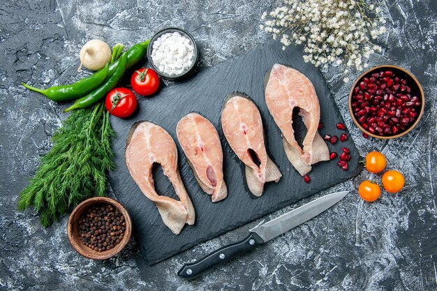 Vue de dessus des tranches de poisson cru sur tableau noir légumes couteau graines de grenade sur table