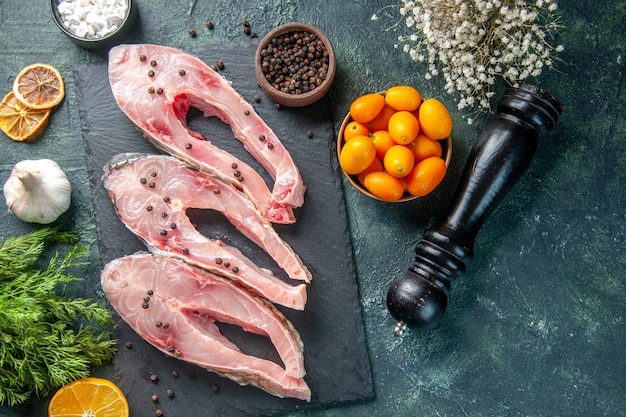 Vue de dessus des tranches de poisson frais avec du poivre sur fond sombre