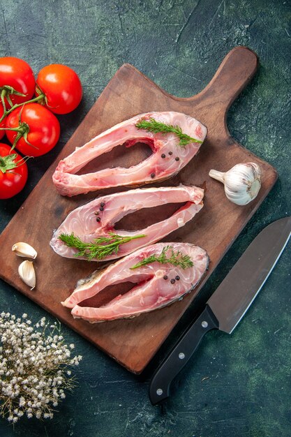 Vue de dessus des tranches de poisson frais avec des tomates sur fond bleu foncé