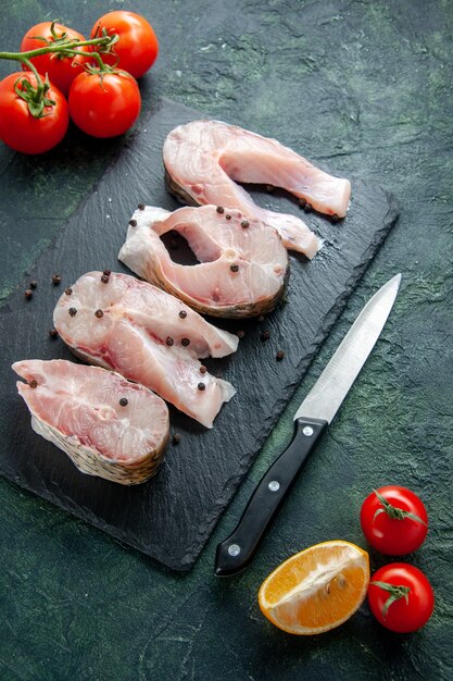 Vue de dessus des tranches de poisson frais avec des tomates rouges sur la paroi sombre de la viande de l'océan de la viande de mer de l'eau alimentaire plat de poivre