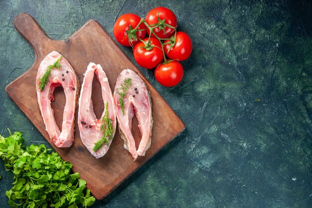 Vue de dessus des tranches de poisson frais avec des tomates et des verts sur fond sombre