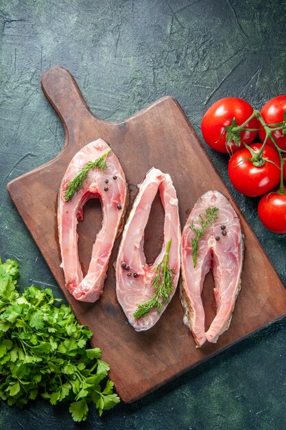 Vue de dessus des tranches de poisson frais avec des tomates et des verts sur fond sombre