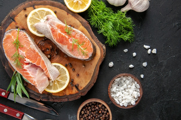 Vue de dessus des tranches de poisson frais avec des tranches de citron et de l'ail sur la table sombre