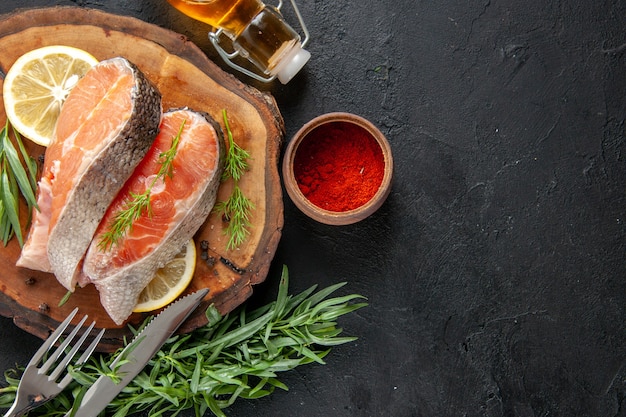 Vue de dessus des tranches de poisson frais avec des tranches de citron et des assaisonnements sur une table sombre