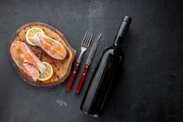 Vue de dessus des tranches de poisson frais avec des tranches de citron et des couverts sur une table sombre