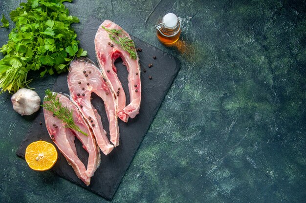 Vue de dessus des tranches de poisson frais avec des verts sur fond sombre