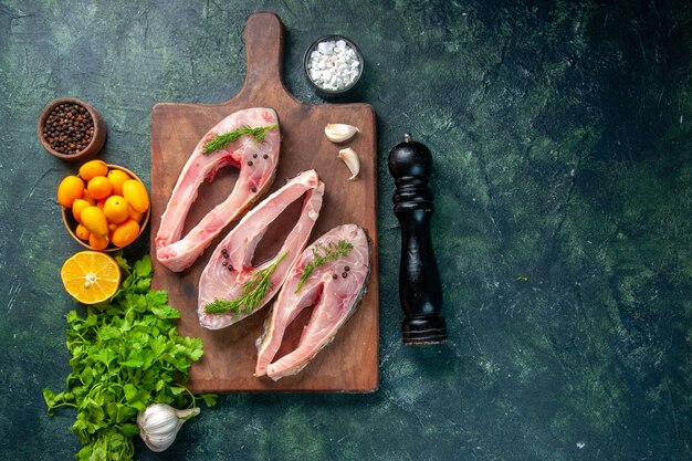 Vue de dessus des tranches de poisson frais avec des verts et des kumquats sur fond sombre