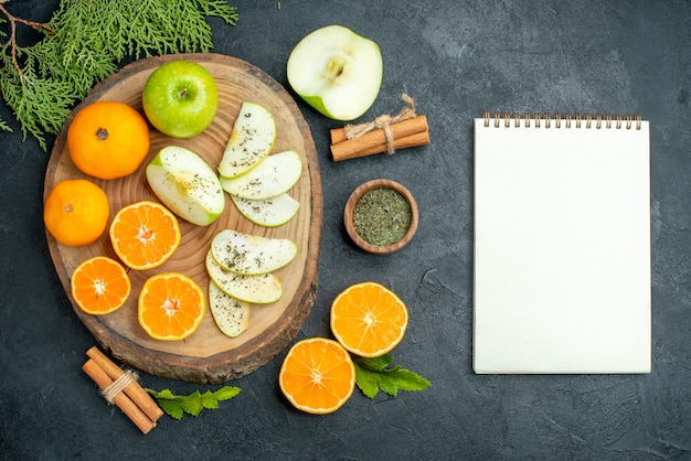 Vue de dessus des tranches de pomme fraîche et d'orange poudre de menthe séchée dans un bol de bâtons de cannelle sur planche de bois