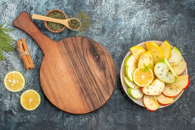 Vue de dessus des tranches de pomme rouge vert jaune frais sur une plaque blanche avec du citron sur une planche à découper en bois limes cannelle sur fond gris